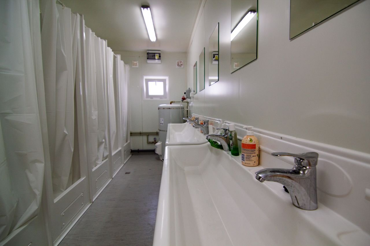 Bright and organized public bathroom features multiple showers and sinks with clean, white surfaces.